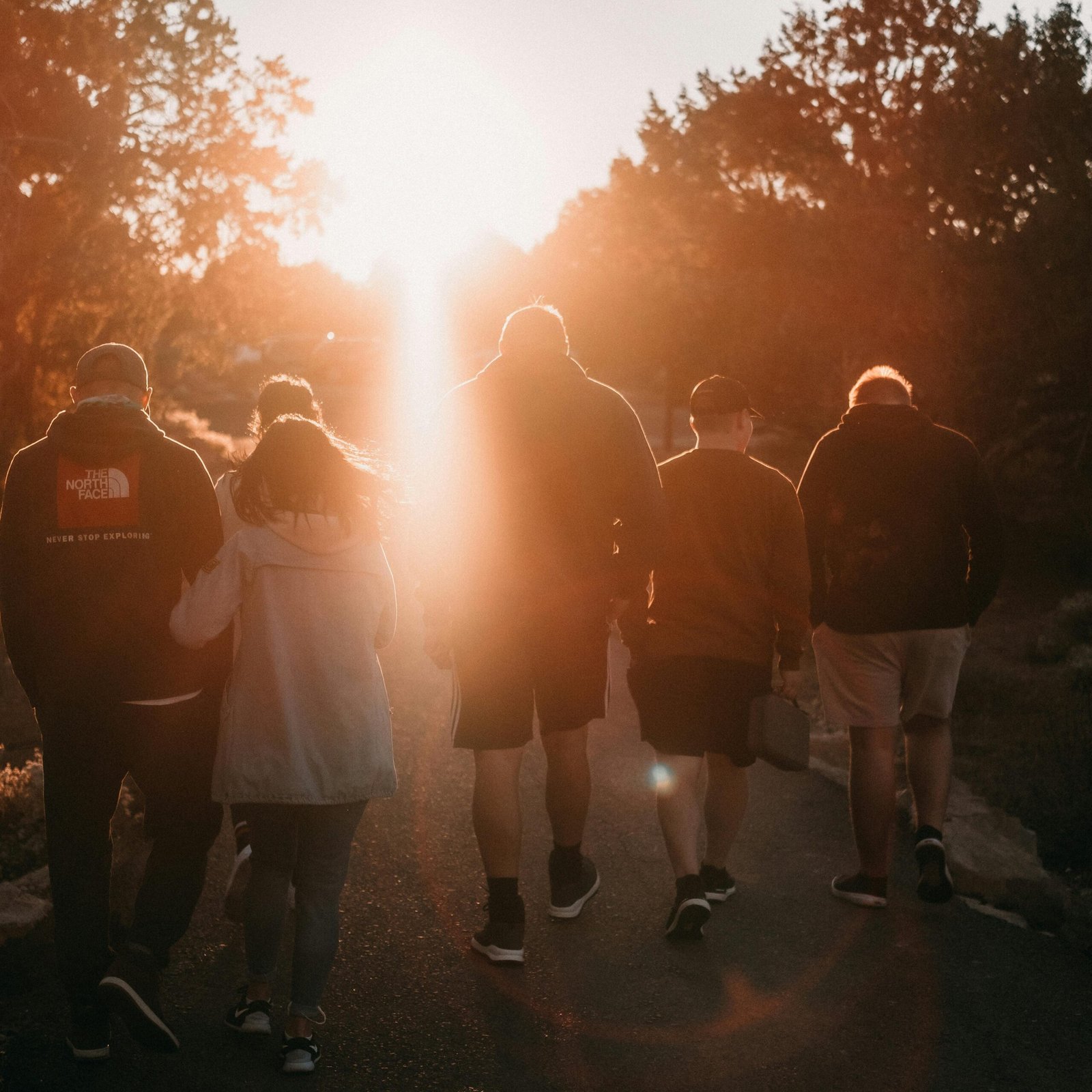 A group of friends strolling on a path during sunset, backlit by warm sunlight.