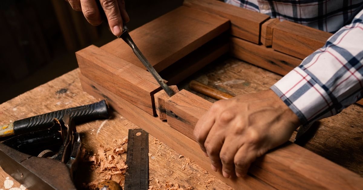 Detailed view of hands using a chisel in woodworking, creating precise craftsmanship.